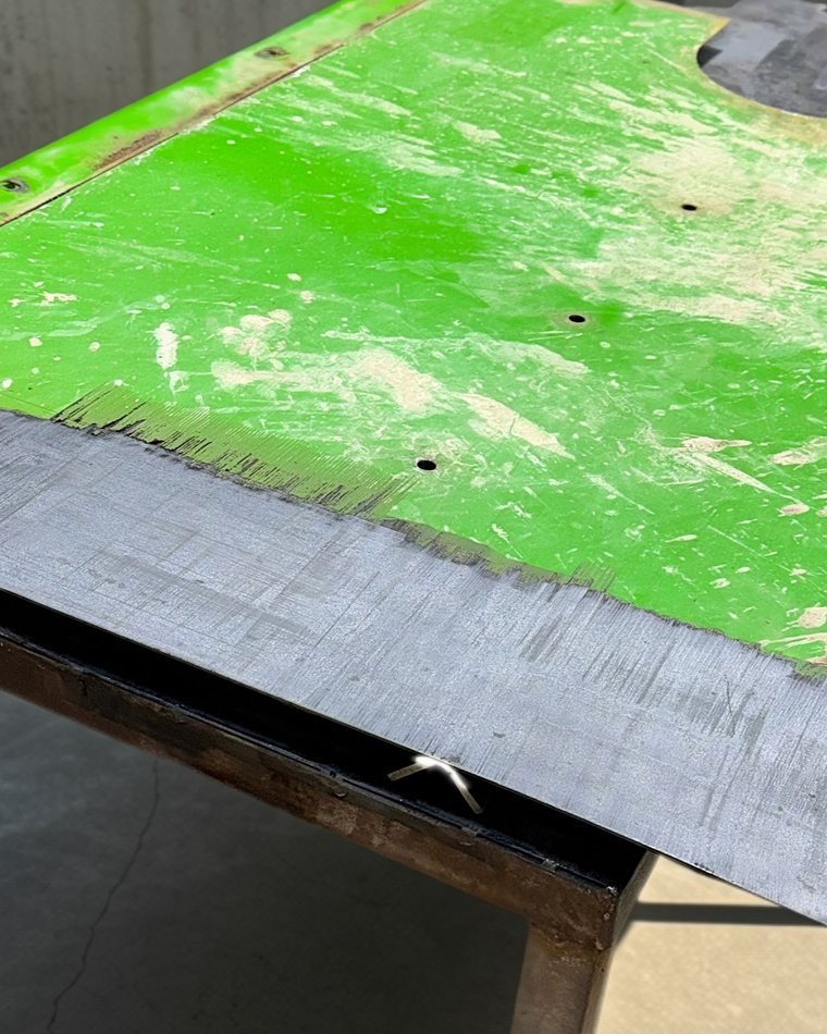John Deere tractor canopy mid-cleaning, with a strip of bare metal where the laser has removed the green paint and dirt